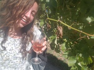 Very happy girl strolls through the rows of vines sipping rosé