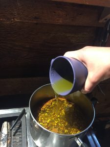 Pouring olive oil into the Cottonwood leaf buds simmering in water.