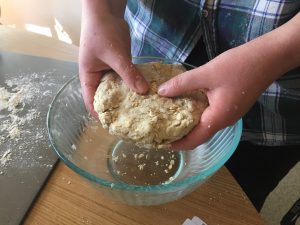 Photo of hands forming dough over a bowl.