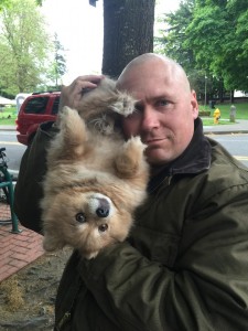 A bald man gently holds a content-looking Pomerian dog upside-down.