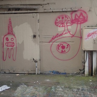 small section of alleyway with childlike graffiti of ghost wearing party hat, and spotted mushrooms